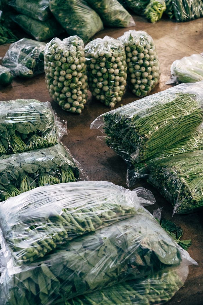 Various fresh green vegetables packed in transparent bags, ready for market sale.